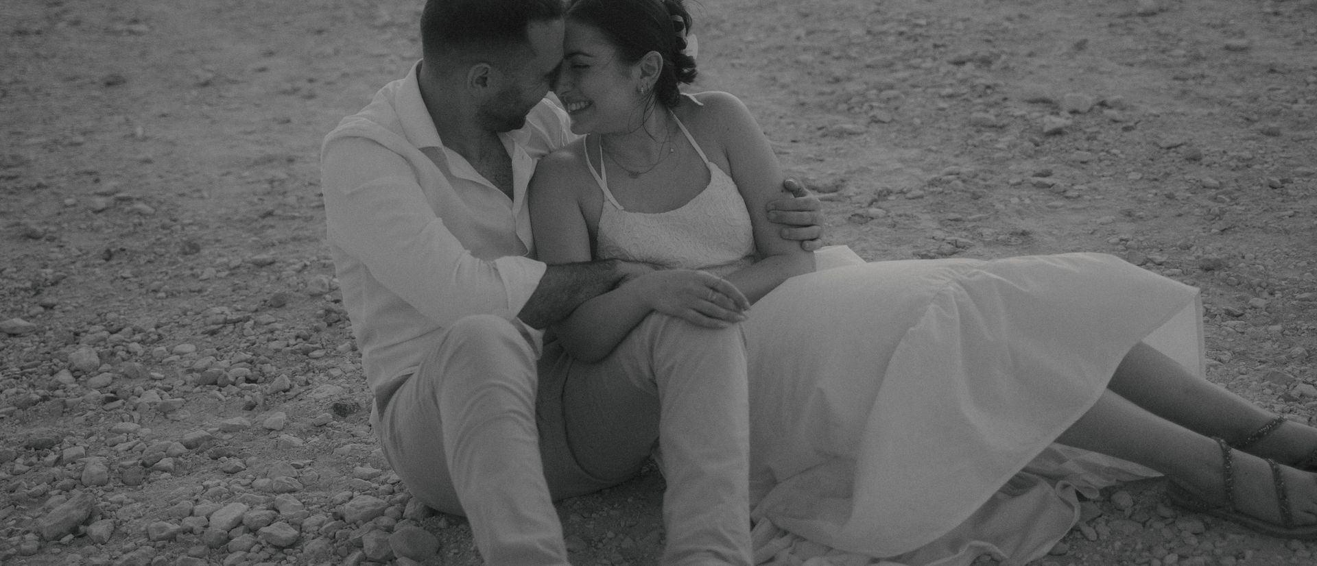 A black and white photograph of a couple laughing, sitting and hugging, enjoying each other&#39;s embrace.