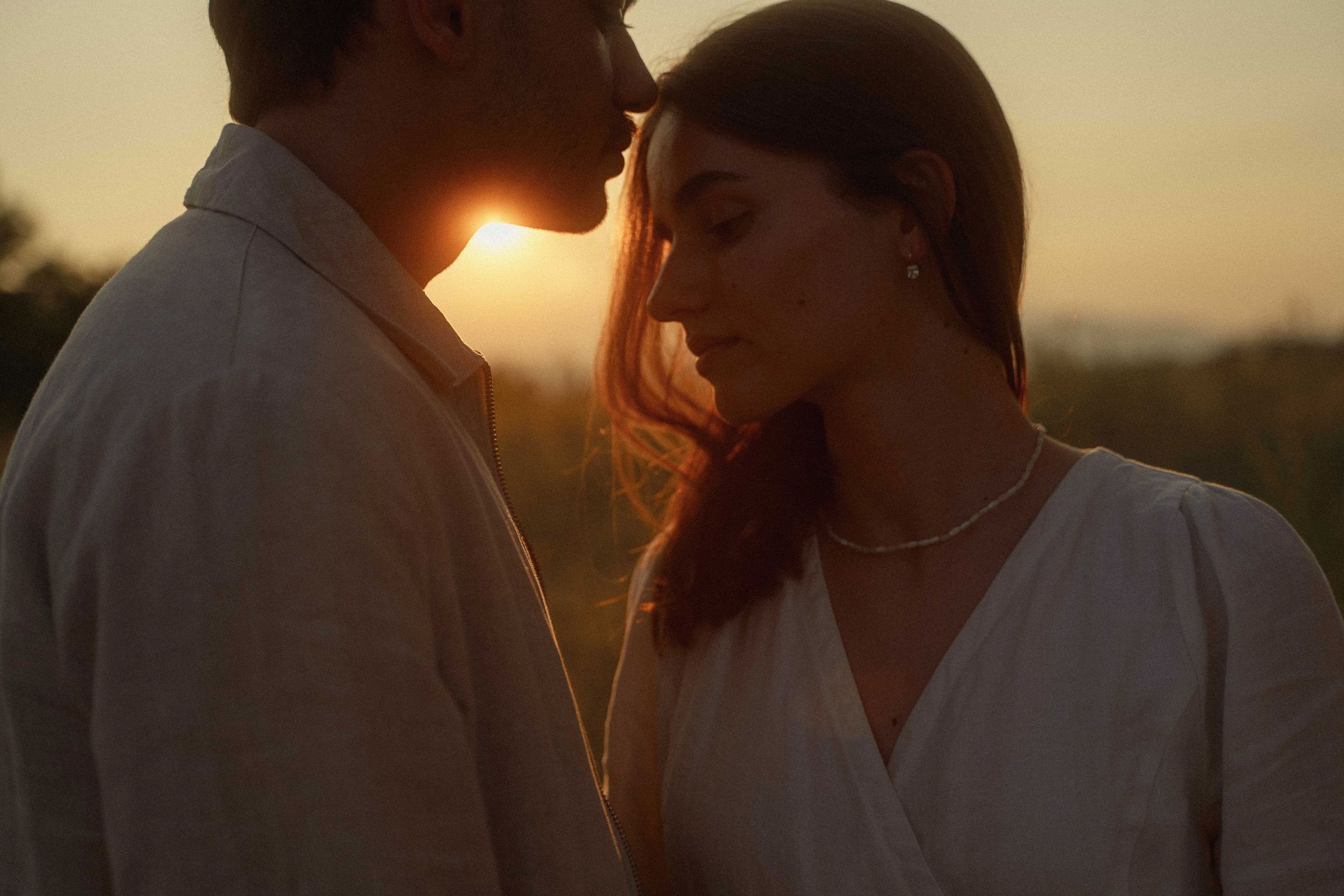 A man kisses his woman on the forehead as the sunset sparks through them