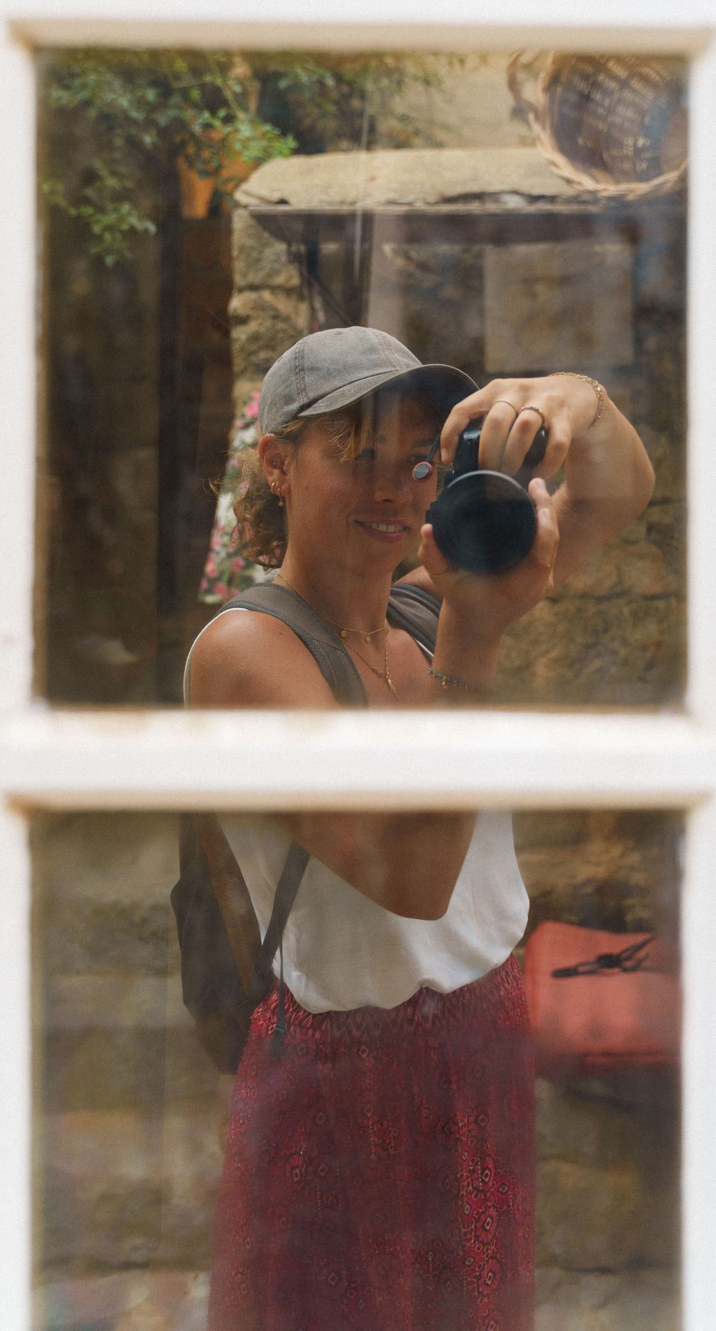 Auto-portrait of a woman holding a camera and smiling into the mirror of a window