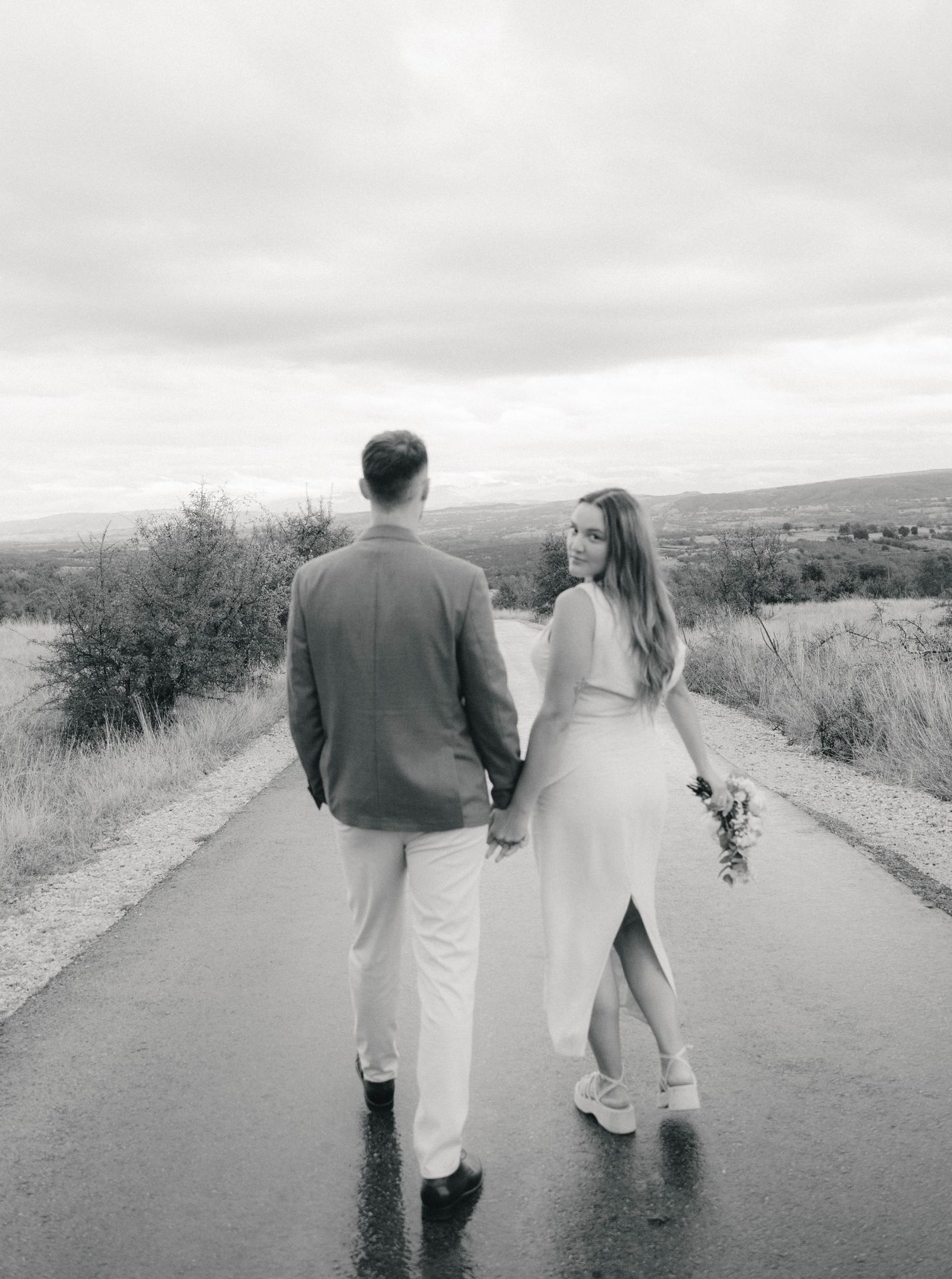 A married couple, black and white photograph, walking hand in hand down an empty road in vast landscape